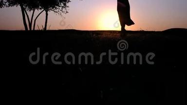 一个年轻美丽的女人在一片发光的草地上朝夕阳走来的剪影